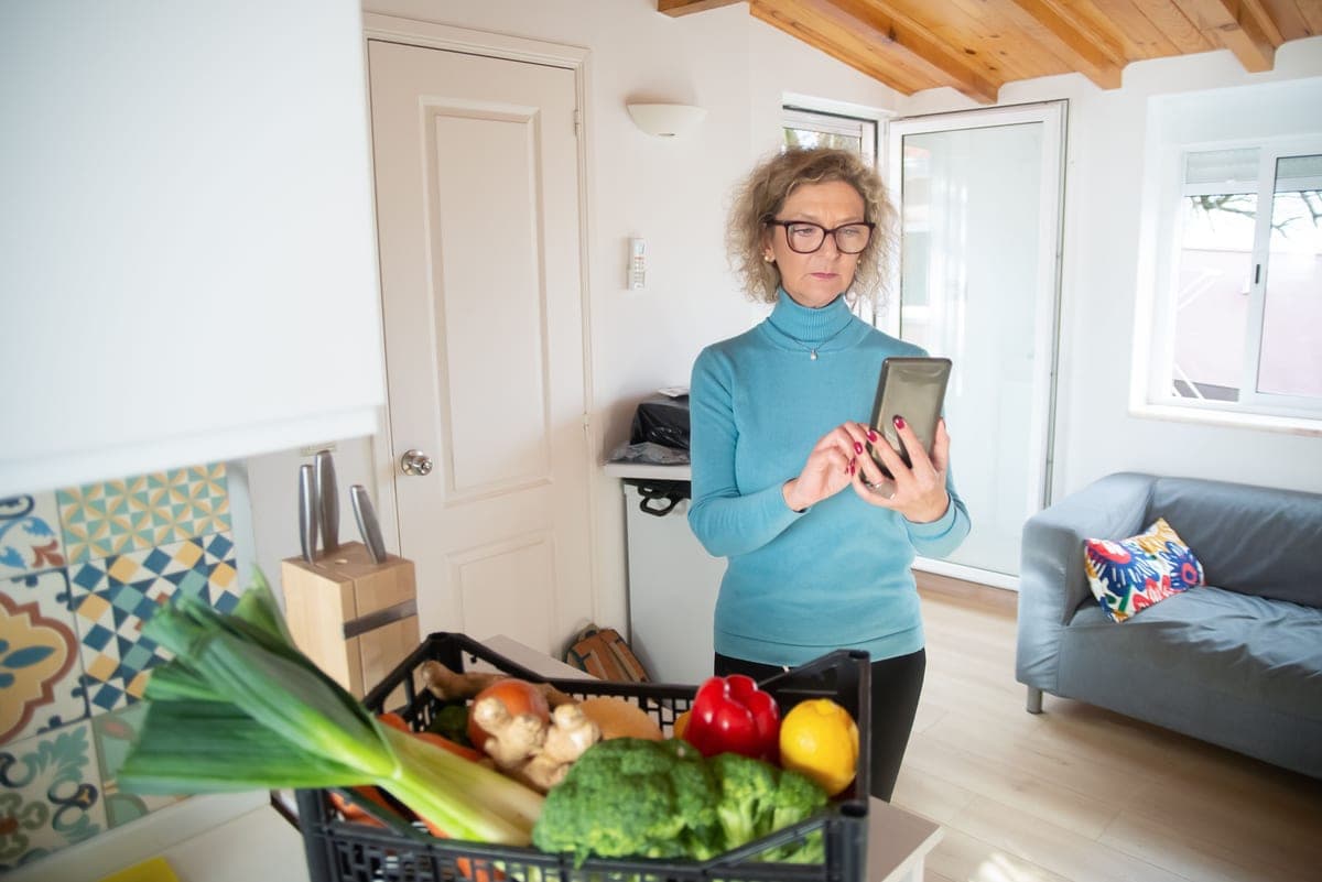 An older woman at home checking her phone in the kitchen