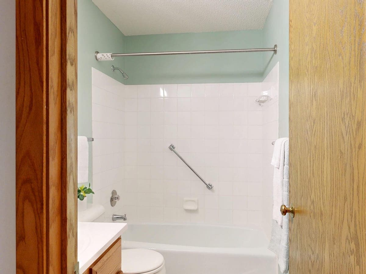 A clean white bathroom with a bathtub and shower rail