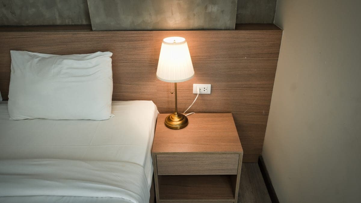A bedside lamp lit on a nightstand beside a bed