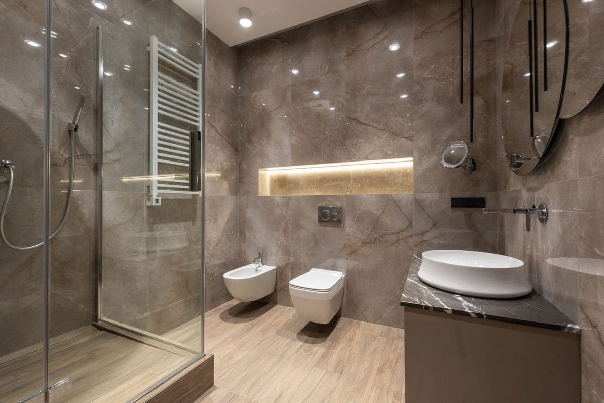 A contemporary bathroom with a toilet and a bidet beside a glass shower