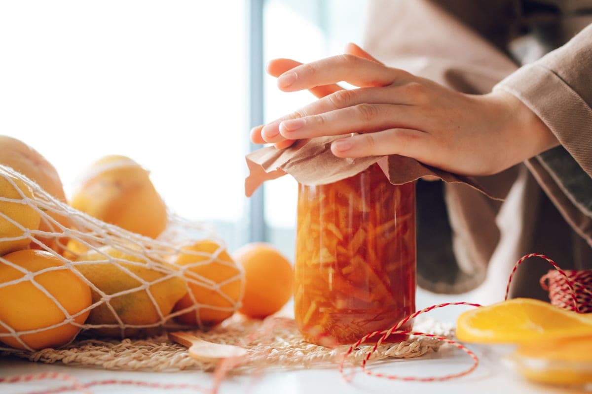 Hands closing a jar of preserves in a sunlit kitchen