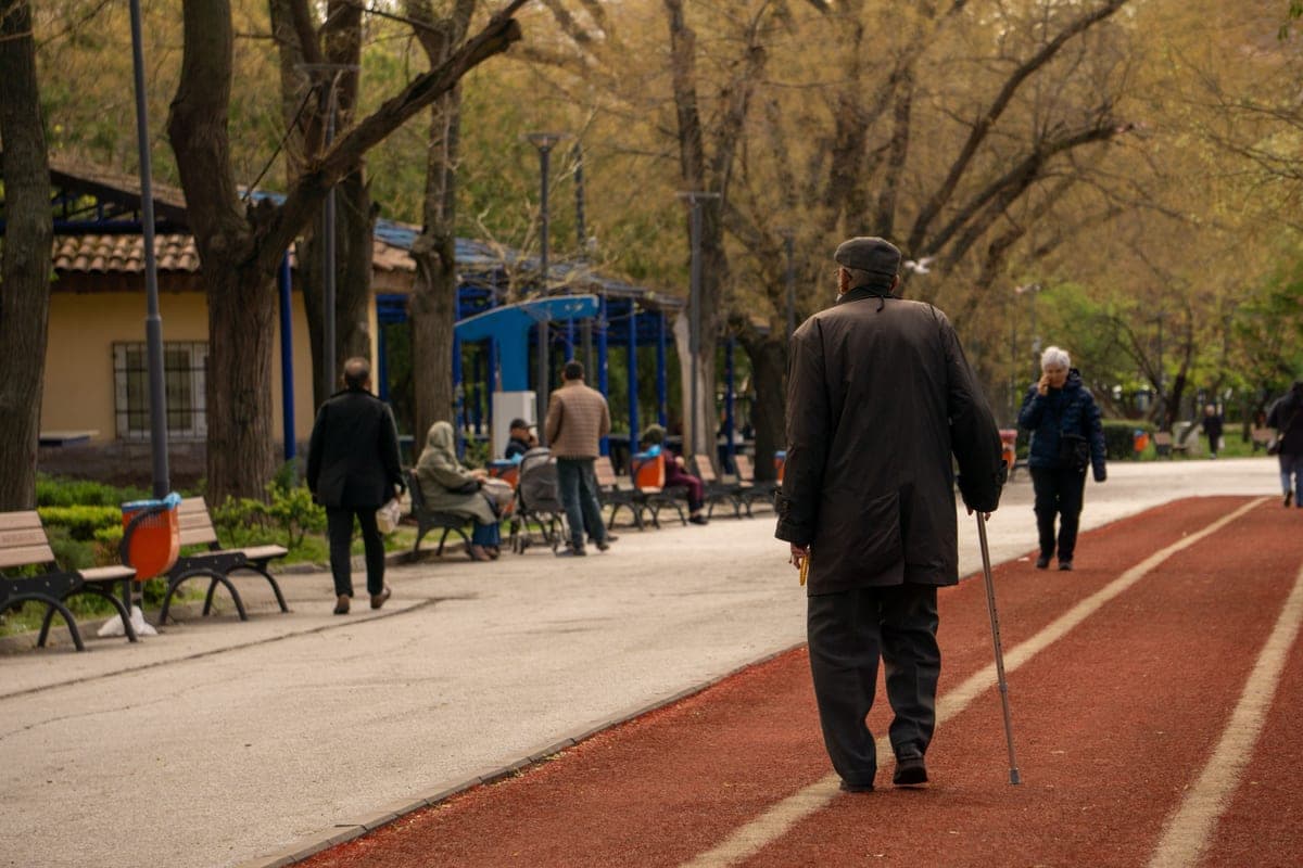 An older man walking with a cane along a park path