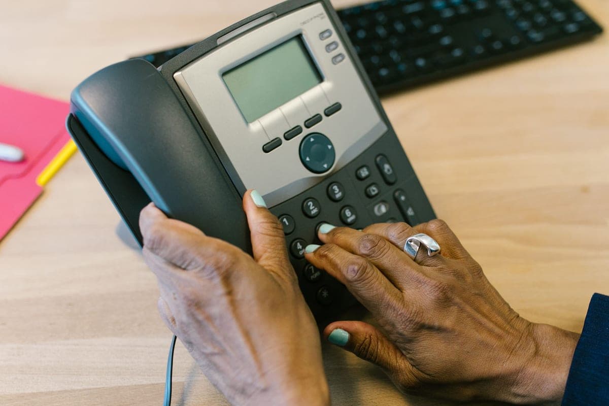 Hands dialing a corded desk telephone