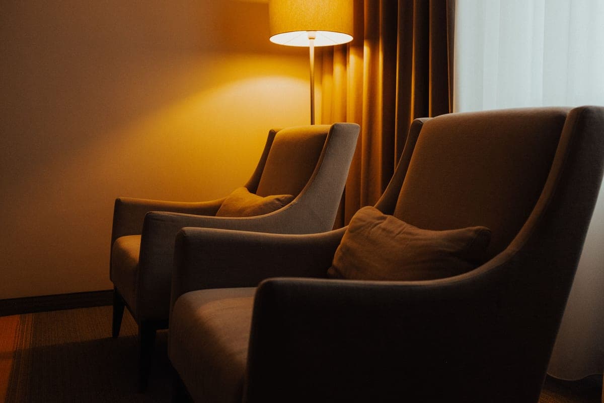 A lit lamp beside two armchairs in a quiet room