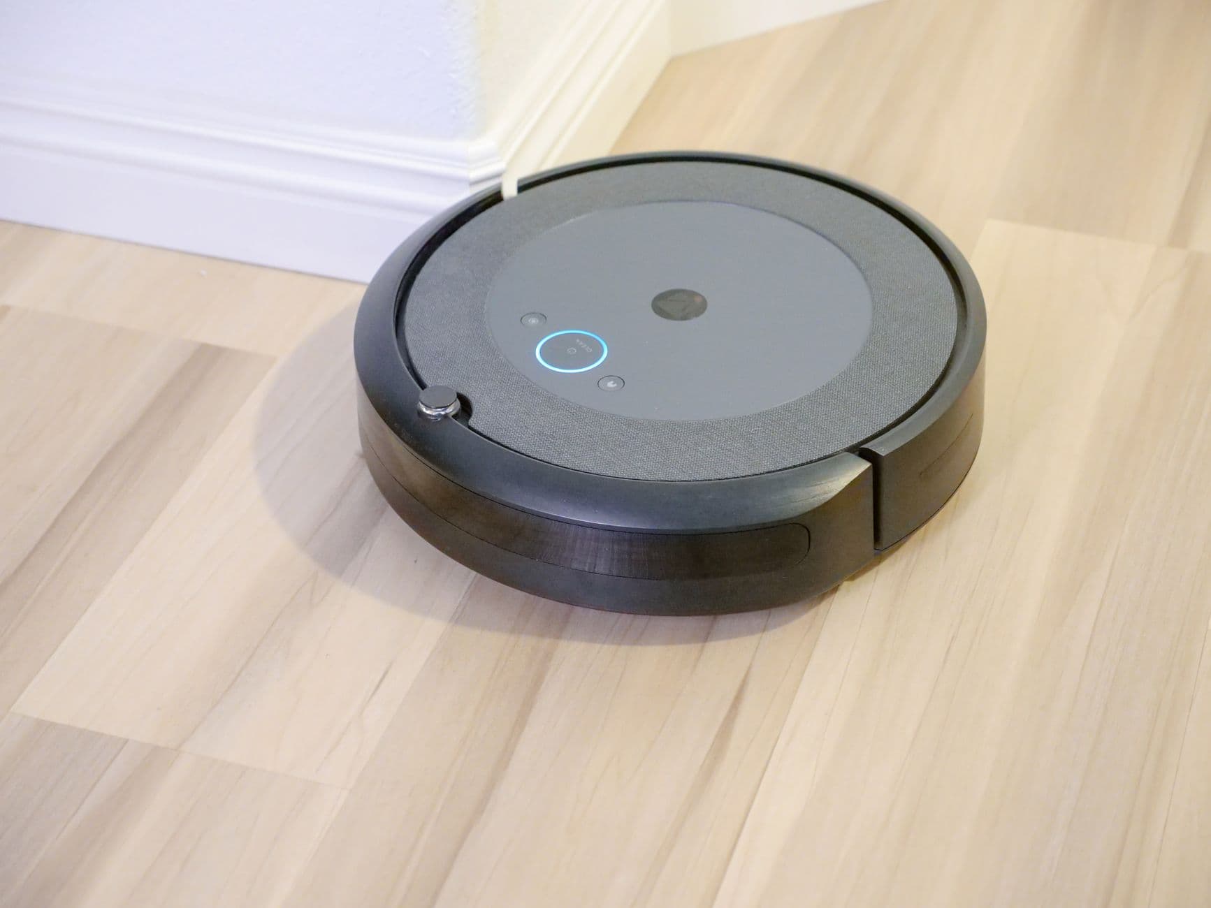 A round robot vacuum with a lit control button on a wooden floor