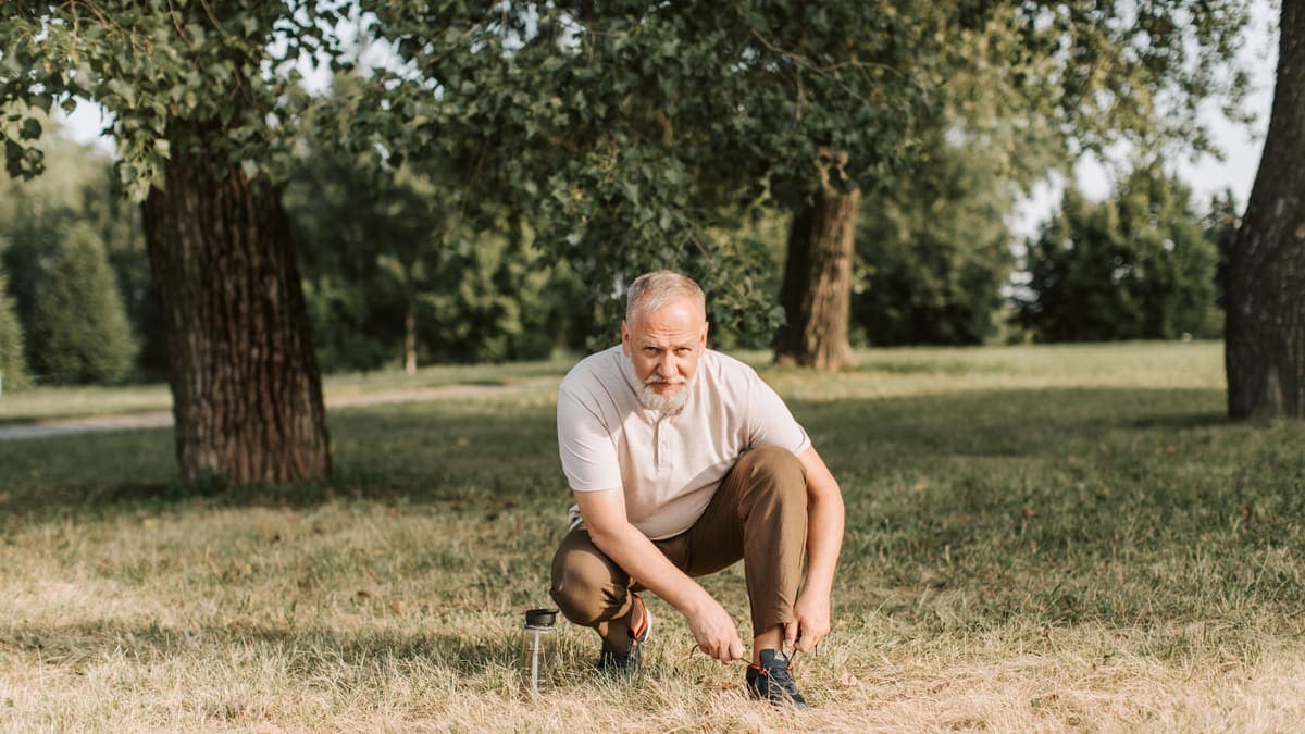An older man in a park crouching down to tie his shoelace