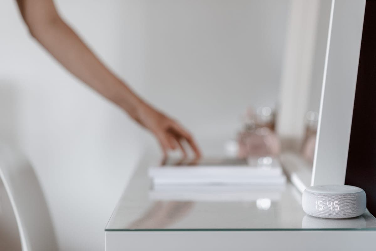 A hand reaching toward a smart speaker on a desk