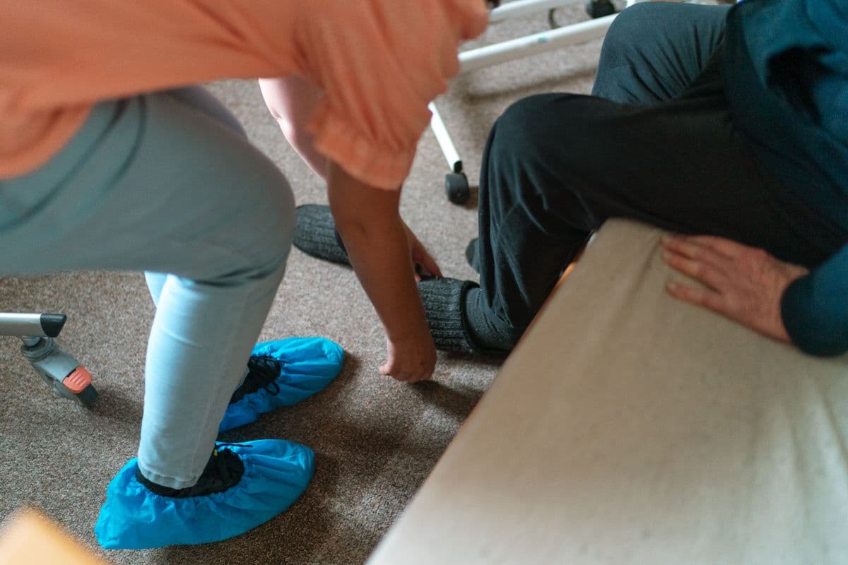 A caregiver helping an older adult put a sock on while seated