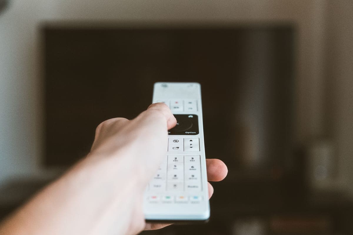 A hand pressing buttons on a television remote
