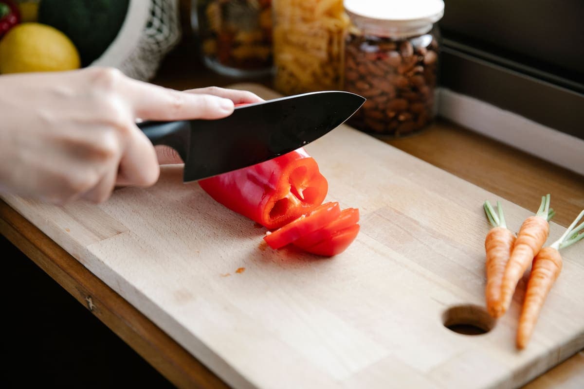 A person slicing a red bell pepper on a chopping board